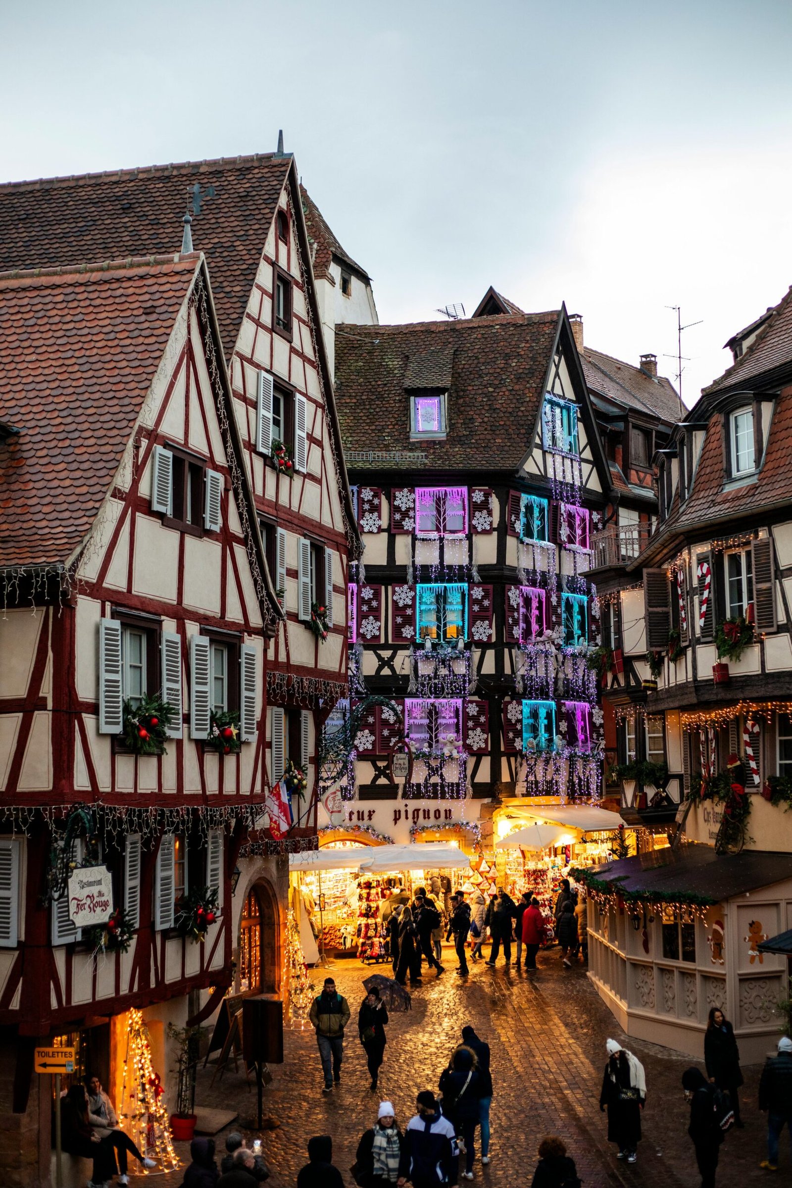 A festive view of Colmar's historic Christmas market with illuminated medieval houses.