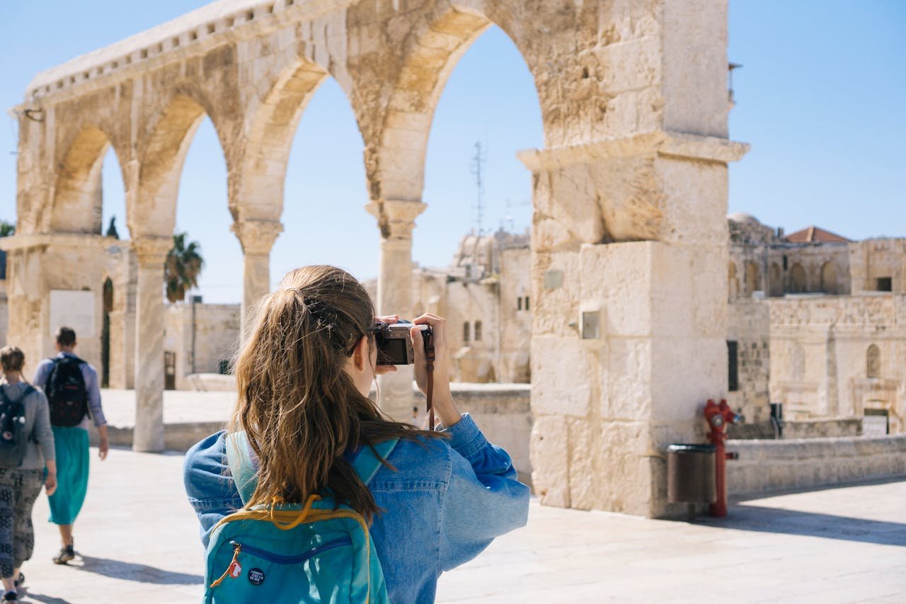 Services-02 A tourist photographs the ancient stone arches in Jerusalem's Old Town, capturing the essence of travel and history.