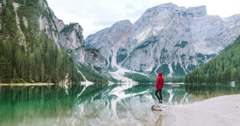 Person standing by the scenic Lake Braies with majestic Dolomite mountains reflected in the water.