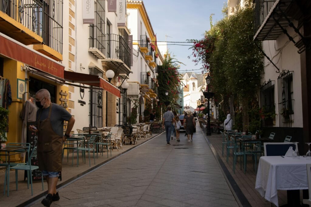 A vibrant street in Marbella, Spain, with people walking past cafes and picturesque buildings.