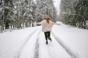 Woman enjoying a carefree walk on a snowy forest road in winter, embracing the serene outdoor setting.