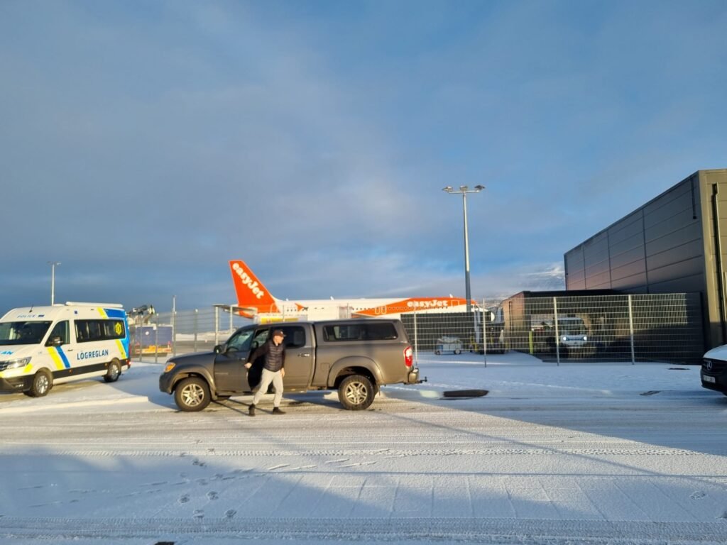 Snowy Akureyri airport with parked vehicles.